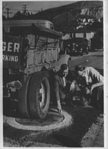 Strength of the wooden manhole covers installed in Los Angeles County, California, is pointed out to Colonel Carl H. Reeves, superintendent of the Los Angeles County, California, Maintenance Department, by Alfred Jones, county surveyor, 1942 (Source: Library of Congress).
